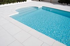 an empty swimming pool with blue water and white tiles on the floor, surrounded by shrubbery