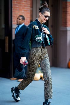 a woman in black jacket and leopard print pants walking down the street with her handbag