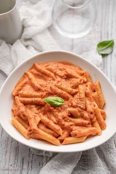 a white bowl filled with pasta and sauce on top of a table next to two wine glasses