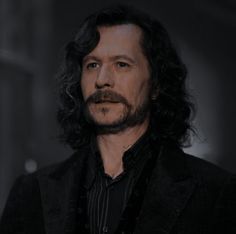 a man with long hair and a beard wearing a black suit in a dark room