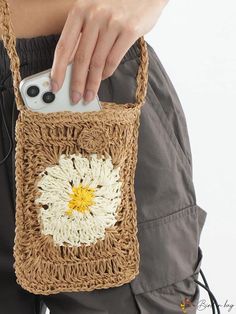 a woman is holding a crocheted bag with a flower on it and an iphone in her hand