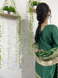 a woman standing in front of a wall with potted plants hanging from it's sides