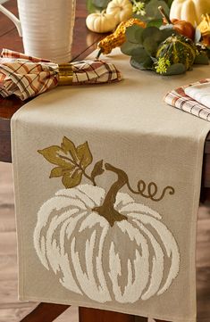 a table topped with a white pumpkin on top of a wooden table covered in fall leaves