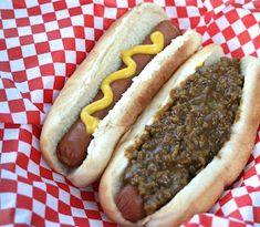 two hotdogs with chili and mustard on a red and white checkered paper