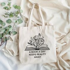 Indulge in literary escapades with our "A Book a Day Keeps Reality Away" tote bag! Perfect for avid book lovers, librarians, and English teachers, this tote isn’t just for carrying your essentials—it’s a whimsical reminder of the joy found in the pages of a good book. Featuring a humorous saying, this bag is ideal for trips to the library, book club meetings, or casual outings. Elevate your reading experience and carry a touch of literary charm wherever you go! Book Totes Diy, Gifts For Book Lovers, Book Tote Bag Aesthetic, Funny Tote Bag Sayings, Bookish Tote Bag, Bookish Tote Bag For Everyday Use, Bookish Tote Bag With Letter Print, Everyday Bookish Tote Canvas Bag, Diy Tote Bag Design