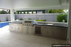 an outdoor kitchen with stainless steel appliances next to a swimming pool and fenced in area