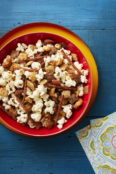 a red bowl filled with popcorn sitting on top of a blue wooden table next to a napkin