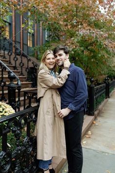 a man and woman standing next to each other in front of a black iron fence