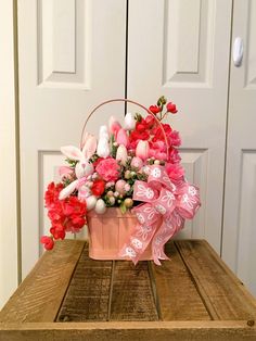 a basket filled with pink and red flowers sitting on top of a wooden table next to a white door