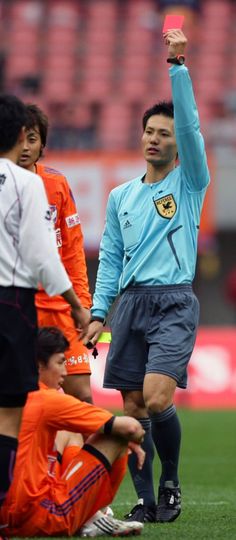 a soccer player is holding up his red card in the air while other players look on