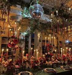 a table set with plates, candles and flowers in front of a disco ball hanging from the ceiling