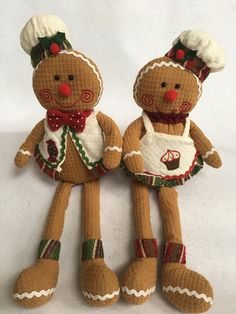 two knitted gingerbread man and woman dolls on a white tablecloth background, one is wearing an apron and the other has a red nose