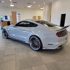 a white mustang parked in a showroom with its hood up and tail lights on