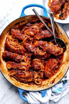 a skillet filled with meat and onions on top of a white counter next to a plate of chicken wings