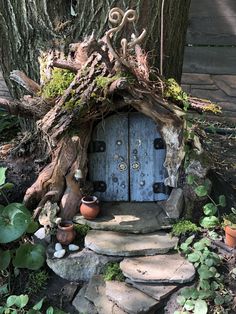 a fairy house made out of branches and rocks in front of a tree with potted plants