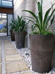 three large planters sitting on top of a stone floor next to a brick wall