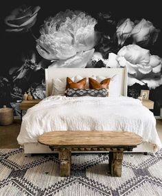 a bedroom with black and white flowers on the wall next to a bed in front of a wooden bench