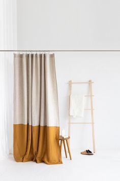 a white room with a brown and beige curtain next to a chair, towel rack and ladder