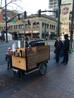 a coffee cart is parked on the side of the street with people standing around it