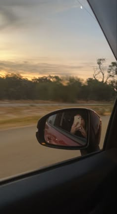 a car's side view mirror with the sun setting in the background