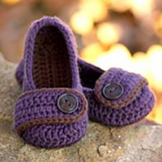 a pair of purple crocheted shoes sitting on top of a rock