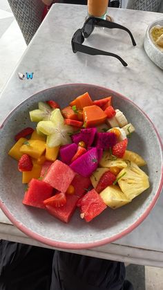 a white bowl filled with cut up fruit on top of a table next to a drink