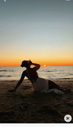 a woman sitting on top of a sandy beach next to the ocean at sun set