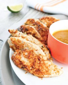 some fried food on a white plate next to a bowl of soup and lime wedges