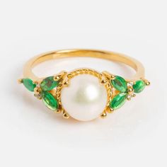 a pearl and emerald ring on a white background