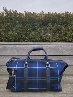 The FH Wadsworth Blue & Black Tartan Leather Duffle Bag is both stylish and functional. Made from imported wool from Scotland, and coupled with blue tumbled leather trim. This modern weekender bag brings luxury, durability, and timelessness to any destination. Interior zipper pocket 100% British Wool Detachable leather strap for shoulder or cross-body wear 21" (Length) x 11" (Height) x 10" (Width) Leather reinforced bottom with heavy duty metal feet Designed in NYC Classic Blue Shoulder Bag For Travel, Blue Satchel With Luggage Sleeve For Travel, Blue Travel Satchel With Luggage Sleeve, Navy Bags With Leather Trim For Everyday Use, Navy Bag With Leather Trim For Everyday, Blue Satchel Weekender Bag For Travel, Navy Rectangular Business Bag, Rectangular Coated Canvas Duffle Bag For Business, Business Weekender Bag With Leather Trim Satchel