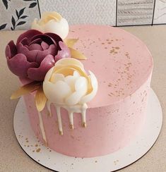 a pink cake with white icing and flowers on top, sitting on a table