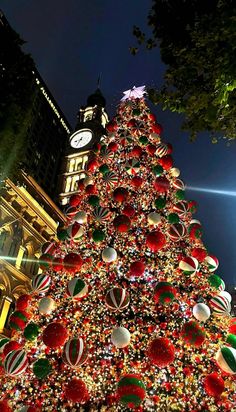 a large christmas tree in the middle of a city at night with lights and ornaments on it