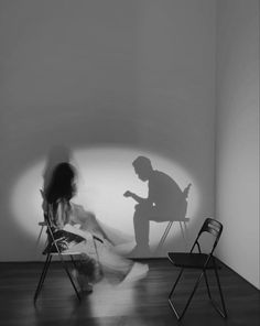 a woman sitting in a chair next to a shadow of a man on the wall