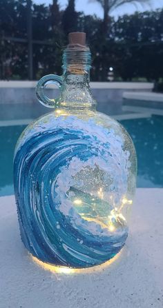 a glass bottle that has some lights in it and is sitting next to a pool