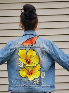 a woman wearing a jean jacket with yellow flowers painted on it and a butterfly flying over her shoulder