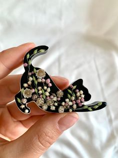 a hand holding a black cat brooch with flowers on it