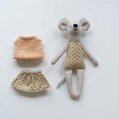 two stuffed animals sitting next to each other on top of a white surface, one wearing a dress and the other with a knitted hat