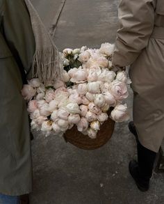 a person is holding a basket full of flowers on the street while another person walks by