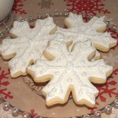 two snowflake cookies sitting on top of a glass plate