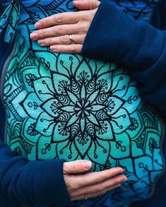 a pregnant woman's belly is adorned with an intricate blue and black design, while her hands are on the stomach