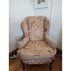 an upholstered chair sits on the floor in front of a wall with a framed picture above it