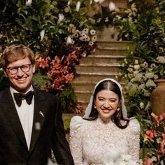 a man and woman standing next to each other in front of a flower filled garden