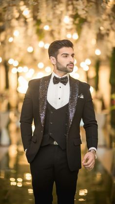 a man wearing a tuxedo and bow tie standing in front of a chandelier