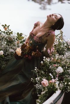 a woman in a green dress is laying down on the ground with flowers around her