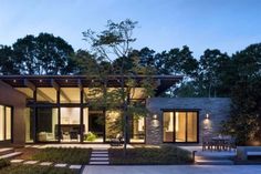 a modern house is lit up at night with lights on the patio and trees in the background