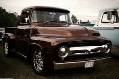 an old truck is parked on the grass near other cars and trucks in the background