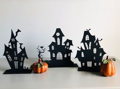 three pumpkins sitting on top of a table next to black paper cut out houses