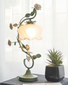 a lamp that is on top of a table next to a potted plant in front of a window