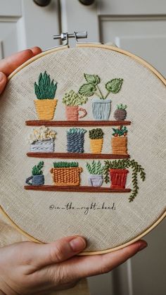 a person holding up a cross - stitch embroidery kit with potted plants on it