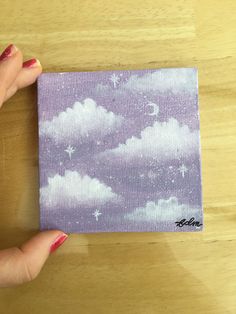 a person holding up a piece of paper with clouds and stars painted on the side